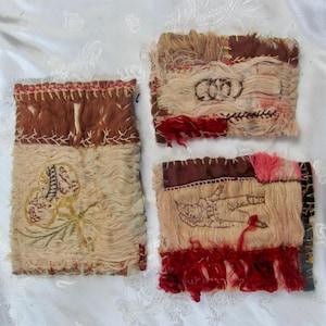 May include: Three handmade textile art pieces with a vintage aesthetic. The pieces feature a mix of brown, beige, and red hues, with embroidered details and fringed edges. The designs include abstract shapes and figures.