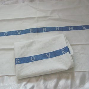 May include: Two white tea towels with blue stripes and the word "GOVERNMENT" embroidered on them.