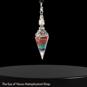 Puede incluir: Un péndulo plateado con un cuerpo de cristal transparente y puntiagudo. El cristal está relleno de capas de piedras rojas, azules y de otros colores. El péndulo está suspendido de una cadena plateada y una parte superior decorativa. The Eye of Venus Metaphysical Shop.