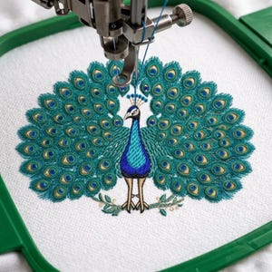 May include: An embroidered peacock with a vibrant teal and blue design, its tail feathers fanned out. The embroidery is in progress, held in a green hoop under a sewing machine needle. The peacock is standing on a green leafy branch.