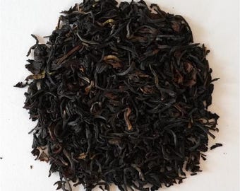 May include: A pile of loose leaf tea, with a dark, rich color. The tea leaves are a deep brown and black, with some lighter reddish-brown highlights. The leaves have a slightly twisted appearance, suggesting a high-quality tea blend.