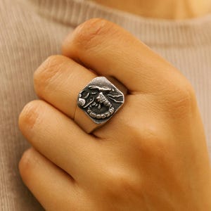 Peut inclure: Une bague en argent ornée d'un motif de scorpion détaillé sur une face carrée. La bague est portée au doigt, mettant en valeur les détails complexes de ce bijou sur le thème du zodiaque. La bague a une finition polie.