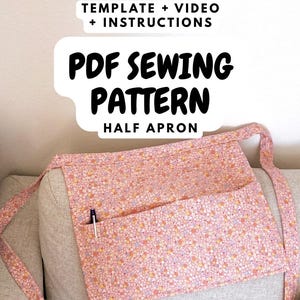 Puede incluir: Un delantal a media cintura rosa floral con un bolsillo, sobre un sofá gris. El delantal tiene correas largas y un bolígrafo en el bolsillo. El texto en la imagen dice "PDF Sewing Pattern" y "Template + Video + Instructions."