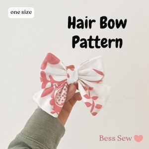 Pode incluir: Um laço de cabelo com padrão floral branco e coral, segurado por uma mão. O texto "Hair Bow Pattern" é exibido em preto, com "one size" em uma caixa branca. O nome da loja "Bess Sew" também é visível.