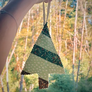 May include: A handmade Christmas tree ornament. The tree is made of fabric with a light green polka dot pattern, a dark green floral pattern, and a brown floral pattern. It has a cream-colored ribbon for hanging.