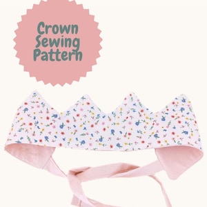 Könnte beinhalten: Ein Schnittmuster für eine Stoffkrone mit rosa Rückseite und Bindebändern. Die Krone ist weiß mit einem Muster aus kleinen rosa, blauen und gelben Blumen. Der Text "Crown Sewing Pattern" befindet sich in einem rosa Kreis.