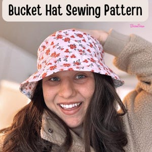 May include: A bucket hat sewing pattern featuring a light pink fabric with a repeating pattern of small red flowers and green leaves. The text "Bucket Hat Sewing Pattern" is displayed at the top, with the brand name "BessSew" in the corner.