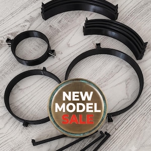 May include: A collection of black circular and curved components, including two circular rings with metal binder clips attached, several curved segments, and straight rods. A circular badge with a bronze finish displays the text NEW MODEL SALE.