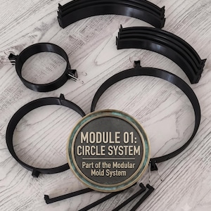 May include: A black modular mold system featuring circular rings, curved segments, and straight connectors. A central circular plaque displays the text: MODULE 01: CIRCLE SYSTEM Part of the Modular Mold System. The components are made of black plastic.