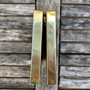 May include: A rectangular brass clutch with a metallic gold finish and a hinged opening. The exterior surface shows visible signs of wear, including light surface scratches and minor tarnishing along the edges of the two metal panels.