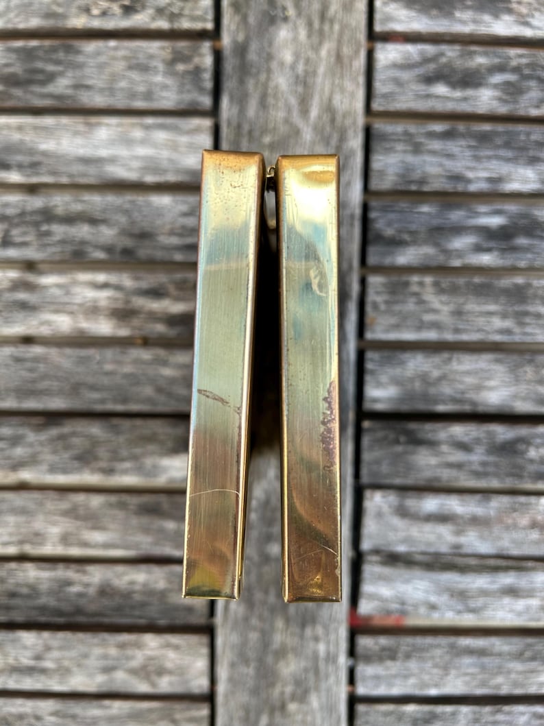 May include: A rectangular brass clutch with a metallic gold finish and a hinged opening. The exterior surface shows visible signs of wear, including light surface scratches and minor tarnishing along the edges of the two metal panels.