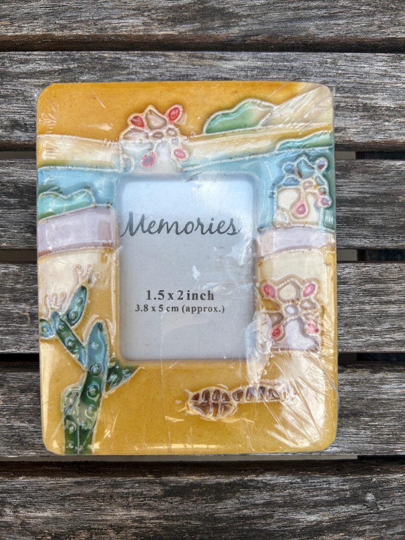 May include: A rectangular yellow picture frame with a raised desert-themed relief featuring a green cactus, pink flowers, and blue accents. The center insert displays the word Memories and the text 1.5 x 2 inch 3.8 x 5 cm (approx.).