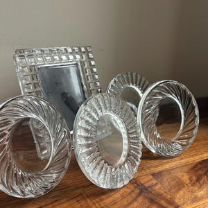 May include: A collection of clear glass items including a rectangular picture frame with a grid-patterned border and three circular glass coasters or decorative pieces featuring distinct radial, swirling, and ribbed textured patterns.