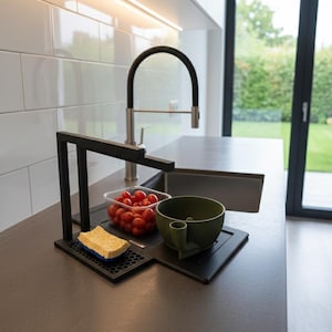 Può includere: Un lavello da cucina moderno con un rubinetto nero e un organizer in metallo nero. L'organizer contiene una spugna, una ciotola verde e un contenitore di pomodorini rossi. Il lavello è in acciaio inossidabile.