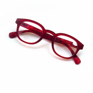 May include: Red-framed eyeglasses with a classic, rounded shape. The frames have a marbled texture, and the lenses are clear. The glasses are set against a white background.