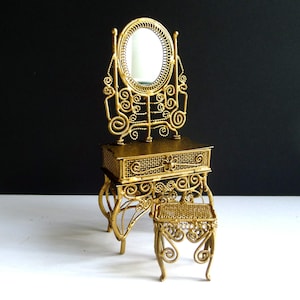 May include: A miniature gold-colored vanity set featuring a table with a mesh drawer and an oval mirror supported by an intricate wire frame, accompanied by a matching small stool with a mesh seat and curved legs, all crafted from metal wire.