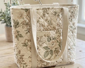 May include: A quilted tote bag featuring a beige and green floral pattern with striped fabric handles and a front pocket. The text Hazel Quilted Tote and Advanced Beginner Sewing Pattern is visible on the image in a brown script and print font.