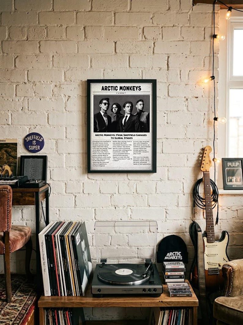 A framed black-and-white poster featuring the band Arctic Monkeys in a newspaper layout hangs on a white brick wall above a record player and an electric guitar.