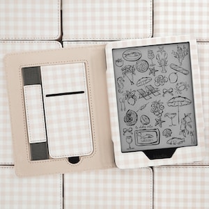 May include: A Kindle e-reader in a light beige and white gingham patterned case. The screen displays a collection of black line art illustrations including seafood, fruit, beach chairs, and a tin labeled Sardines with the text la dolce vita.