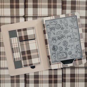 Könnte beinhalten: Eine geöffnete E-Reader-Hülle mit einem braun-beige-weißen Karomuster. Das Innere ist hellbeige gefüttert und verfügt über ein Einsteckfach sowie eine Schlaufe. Das Display zeigt schwarze Strichzeichnungen von Lebensmitteln und Meeresmotiven.