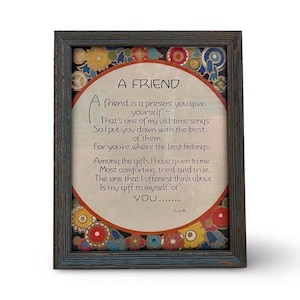 May include: A framed print featuring the poem A FRIEND in black text on a cream background, enclosed in a circular red border. The corners are decorated with colorful circular patterns. The frame is dark, weathered wood with a blue-grey finish.