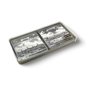 Puede incluir: Una caja rectangular de plástico transparente con un marco de metal plateado. En el interior hay dos grabados de paisajes en blanco y negro de ciudades. Los grabados están etiquetados como "Lübeck" y "Flensburg". Una pequeña etiqueta dorada dice "SCHNEIDER".