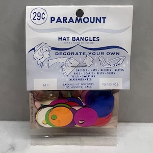 May include: A packet of Paramount Hat Bangles, containing colourful, circular decorations. The packaging features the text "Decorate Your Own" and lists items such as dresses, hats, and gloves. The price is marked as 29¢.