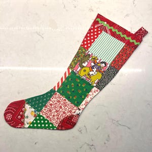 May include: A patchwork Christmas stocking with a variety of fabric patterns. The stocking features red polka dots, green floral, and a cowboy and horse illustration. The top edge has a green zigzag trim.