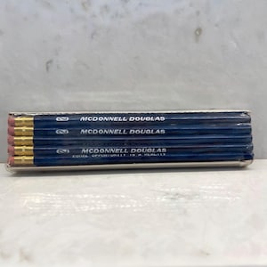 May include: A package of pencils with the text "McDonnell Douglas" printed on the blue barrels. The pencils have gold-colored metal bands and pink erasers. The text "Equal Opportunity Is A Reality" is printed on one pencil.
