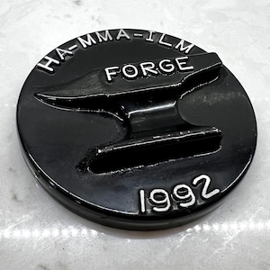 May include: Black round metal disc with a raised image of an anvil and the text "HA-MMA-ILM FORGE 1992".