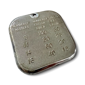 May include: A vintage silver-toned needle and thread gauge. The gauge has text that reads "NUMBER OF NEEDLES" and "NUMBER OF THREAD" with corresponding numbers for cotton, linen, silk, and rayon threads. The gauge has a small hole at the top.