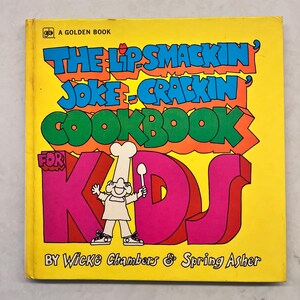 Op de afbeelding: Een gele, oranje, groene, roze en rode boekomslag met de titel "The Lipsmackin' Joke-Crackin' Cookbook for Kids" en de namen van de auteurs "Wicke Chambers & Spring Asher".