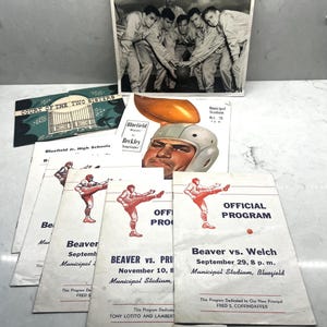 Puede incluir: Una colección de recuerdos deportivos antiguos, que incluye programas de partidos de fútbol y una fotografía en blanco y negro de un equipo de fútbol. Los programas presentan ilustraciones de jugadores de fútbol y detalles del juego.