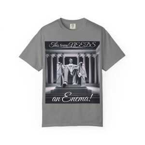 May include: Gray t-shirt featuring a black and white image of the Lincoln Memorial with Abraham Lincoln seated. The text "This town NEEDS an Enema!" is displayed below the image.