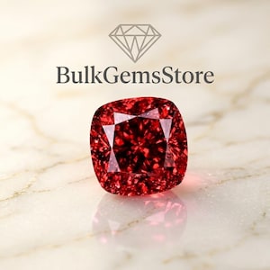 May include: A cushion-cut red gemstone with a faceted surface that reflects light. Above the gemstone, the text BulkGemsStore is displayed in a dark gray font, accompanied by a diamond-shaped icon featuring a geometric line design.