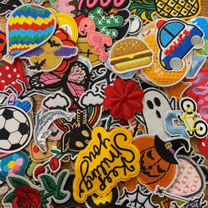 Peut inclure: Un assortiment de patchs brodés de différentes formes et couleurs. Les motifs incluent une montgolfière, un flamant rose, un hamburger, une voiture de police, un ballon de foot, un fantôme et un patch avec l'inscription "Keep Smiling".