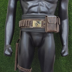 May include: A brown leather belt with a gold buckle and a matching pouch and holster. The belt has multiple loops for holding items. A leg strap is also included. The mannequin is standing on a green surface.