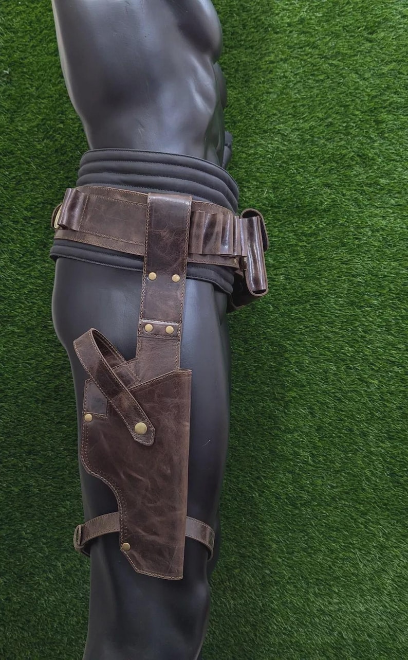 May include: Brown leather holster and belt set. The holster is attached to a leg strap and the belt has multiple pouches. The leather has a distressed look with brass-coloured rivets. The items are displayed on a black mannequin against a green background.