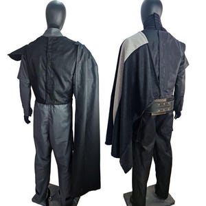 May include: Two mannequins display a dark gray costume with a black cape and a wide belt. The costume includes a long-sleeved shirt, pants, and a cape that drapes over the shoulder. The belt has metal grommets.