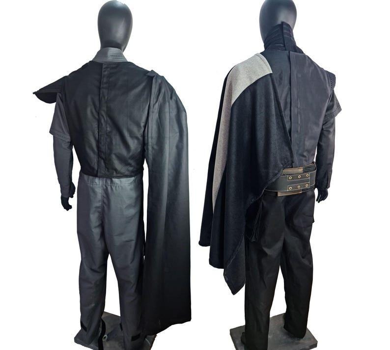 May include: Two mannequins display a dark gray costume with a black cape and a wide belt. The costume includes a long-sleeved shirt, pants, and a cape that drapes over the shoulder. The belt has metal grommets.
