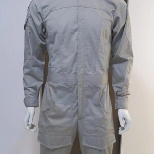 Pu&ograve; includere: Tuta grigio chiaro esposta su un manichino. L'indumento intero presenta un collo alto, maniche lunghe, tasche multiple e una vestibilit&agrave; su misura. Il manichino &egrave; bianco e si trova su uno sfondo neutro.