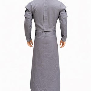 Puede incluir: Un disfraz gris con cuello alto, mangas largas y una parte inferior larga tipo falda. El disfraz tiene un cintur&oacute;n en la cintura y detalles negros en los hombros. El atuendo se muestra en un maniqu&iacute;.