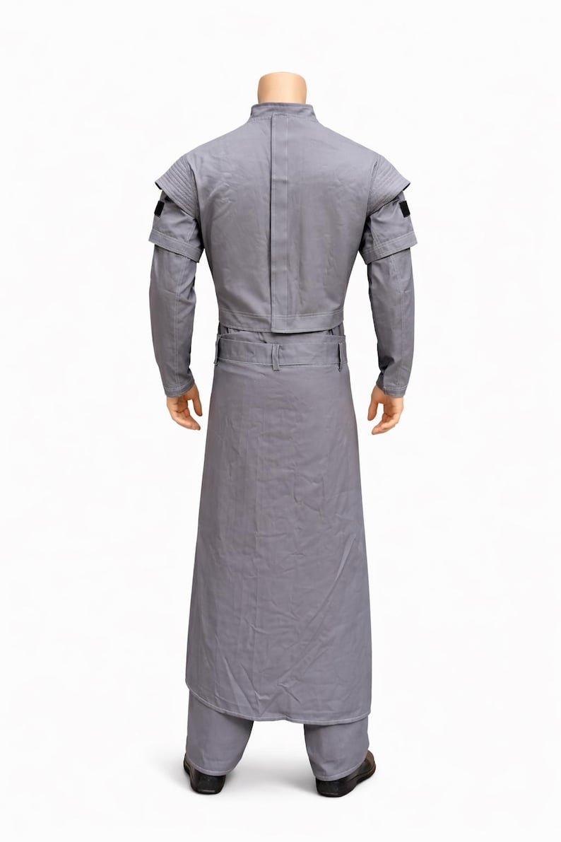 Puede incluir: Un disfraz gris con cuello alto, mangas largas y una parte inferior larga tipo falda. El disfraz tiene un cintur&oacute;n en la cintura y detalles negros en los hombros. El atuendo se muestra en un maniqu&iacute;.