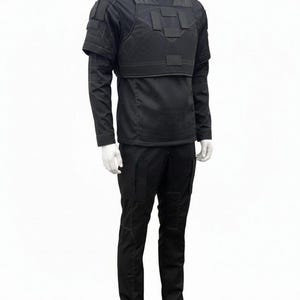 May include: A black tactical outfit displayed on a mannequin. The outfit includes a high-neck shirt, a vest with multiple panels, and cargo pants. The vest has shoulder pads and a horizontal strap across the chest. The pants have multiple pockets.