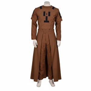 Puede incluir: Un disfraz marr&oacute;n exhibido en un maniqu&iacute;. El atuendo incluye una parte superior de manga larga con detalles negros y una parte inferior larga similar a una falda a juego. La parte superior presenta un dise&ntilde;o negro &uacute;nico en el pecho.
