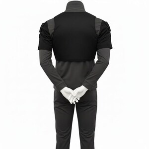 May include: Black vest with short sleeves and shoulder details, worn over a long-sleeved grey shirt. The model is wearing matching grey trousers. The hands are clasped in front. The outfit is displayed against a white background.