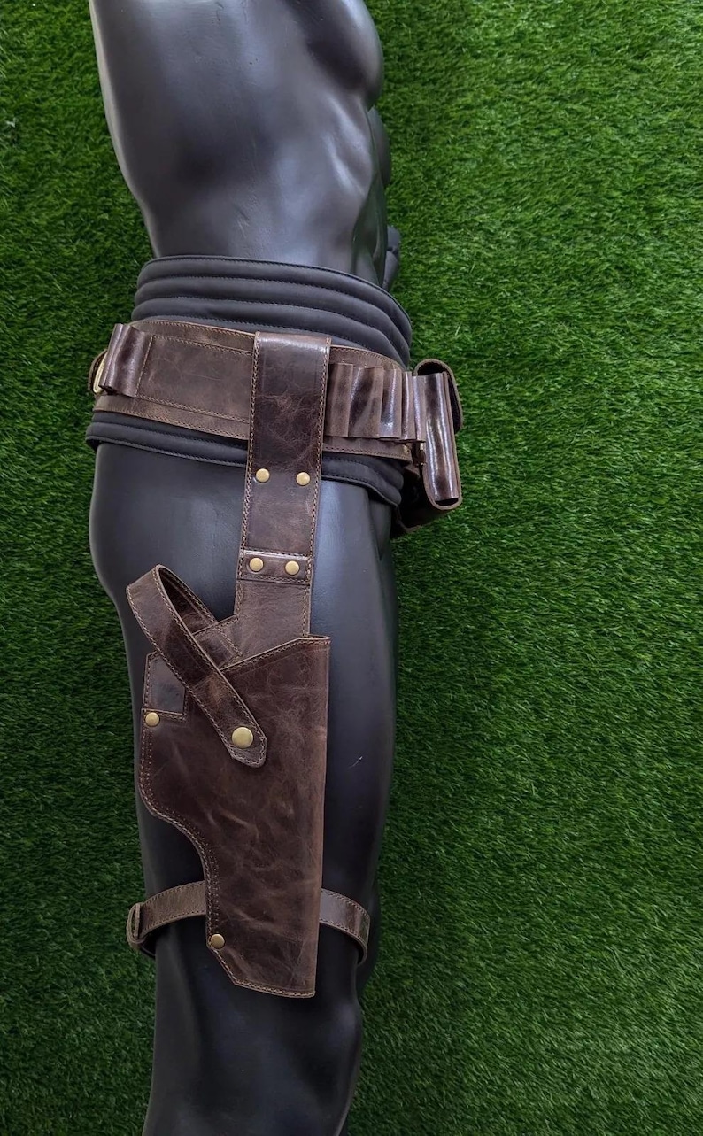 May include: A brown leather holster and belt set. The holster is attached to a leg strap and the belt has multiple pouches. The set is displayed on a black mannequin against a green background.