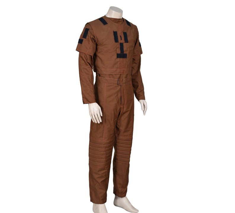 Puede incluir: Un mono marr&oacute;n con detalles negros en los hombros y el pecho. La parte superior de manga larga es corta y los pantalones tienen secciones acolchadas en las rodillas. El atuendo se muestra en un maniqu&iacute;.