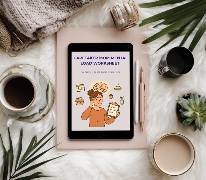 May include: A digital tablet displays a worksheet titled "Caretaker Mom Mental Load Worksheet" with illustrations. The tablet is on a light pink surface, surrounded by a cup of coffee, a pen, and decorative items, all set against a fluffy white background.