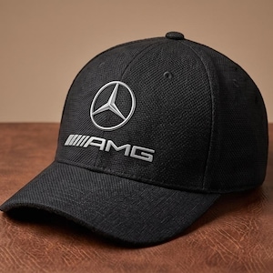 Op de afbeelding: Zwarte baseballcap met het zilveren AMG-logo. De cap heeft een gebogen klep en een gestructureerde kroon. Het AMG-logo toont een driepuntige ster in een cirkel, met de letters "AMG" eronder.